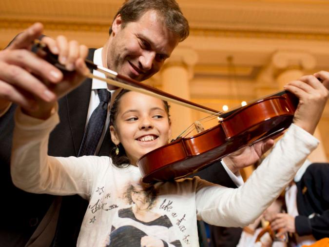 Ein Mädchen spielt auf einer Geige, ein Mann gibt Hilfestellung