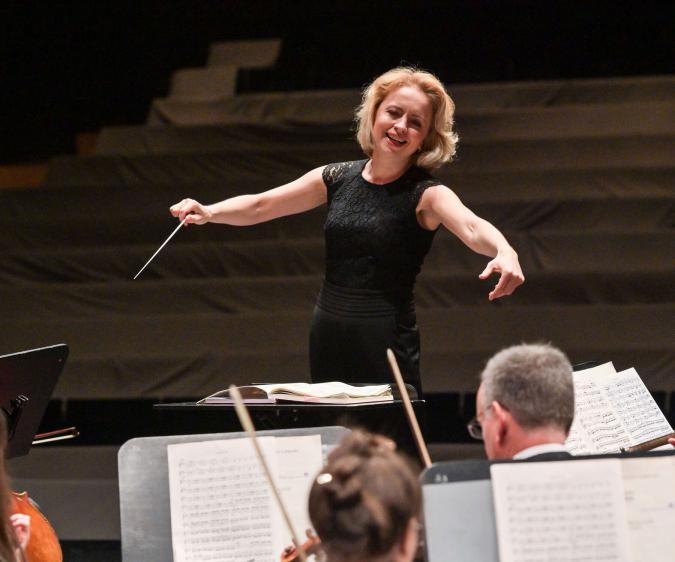 Eine blonde Frau dirigiert ein Orchester