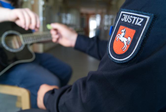 Ein niedersächsischer Justizvollzugsbeamte reicht Häftling mit Gitarre ein Plektrum