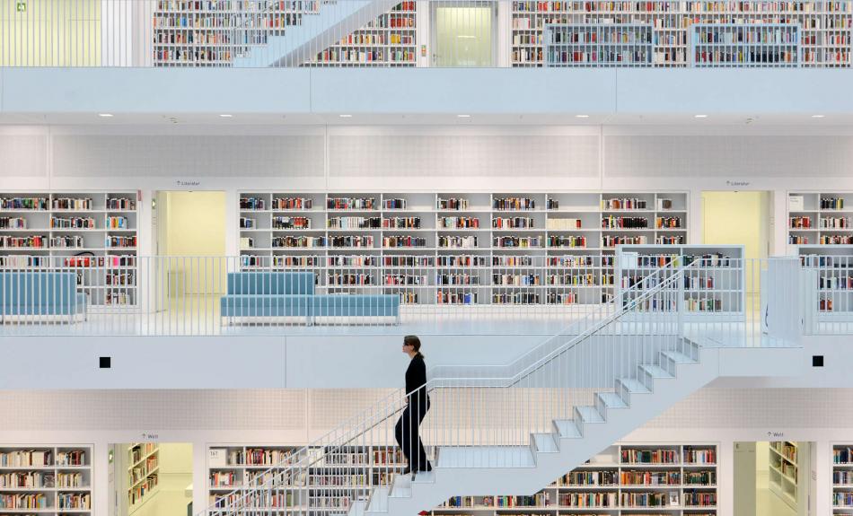 Ein heller Bibliotheksraum mit mehreren Ebenen, eine Frau geht eine Treppe herunter