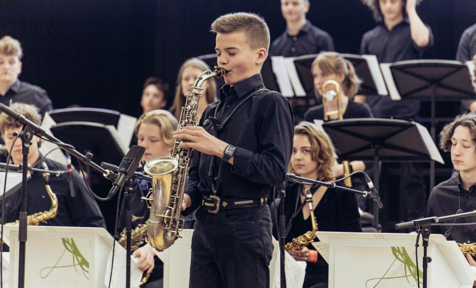 Junger Saxofonist spielt bei Auftritt, im Hintergrund Jazzorchester