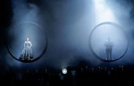 Eine Szene auf einer Opernbühne mit zwei Figuren, die in großen Ringen über der Bühne schweben