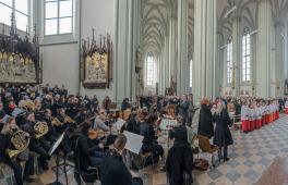 Links im Bild ein Orchester mit musikalischem Leiter und rechts im Bild die Gemeinde und Messdiener während eines Gottesdiensts in der Heilig-Kreuz-Kirche Giesing.