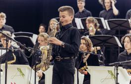 Junger Saxofonist spielt bei Auftritt, im Hintergrund Jazzorchester