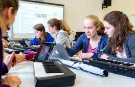 Mädchen mit Keyboards, Tablets und Kopfhörern in einem Klassenraum