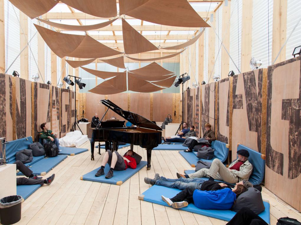 Pianist spielt in einem Raum mit zahlreichen Matten, auf denen Personen Platz genommen haben