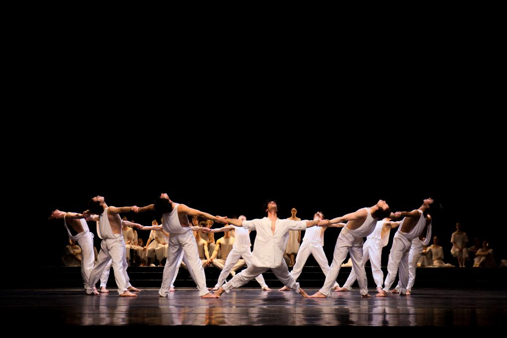 Inszenierung der Matthäus-Passion am Hamburg Ballett. Zwölf weiß gekleideten Tänzer auf der schwarzen Bühne halten sich an den Händen und bilden einen weiten Kreis.