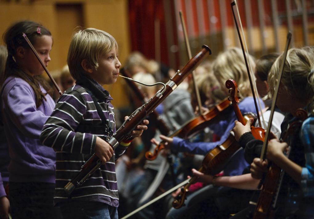 Kinder während einer Orchesterprobe, Junge mit Fagott im Zentrum, weitere Kinder mit Geigen